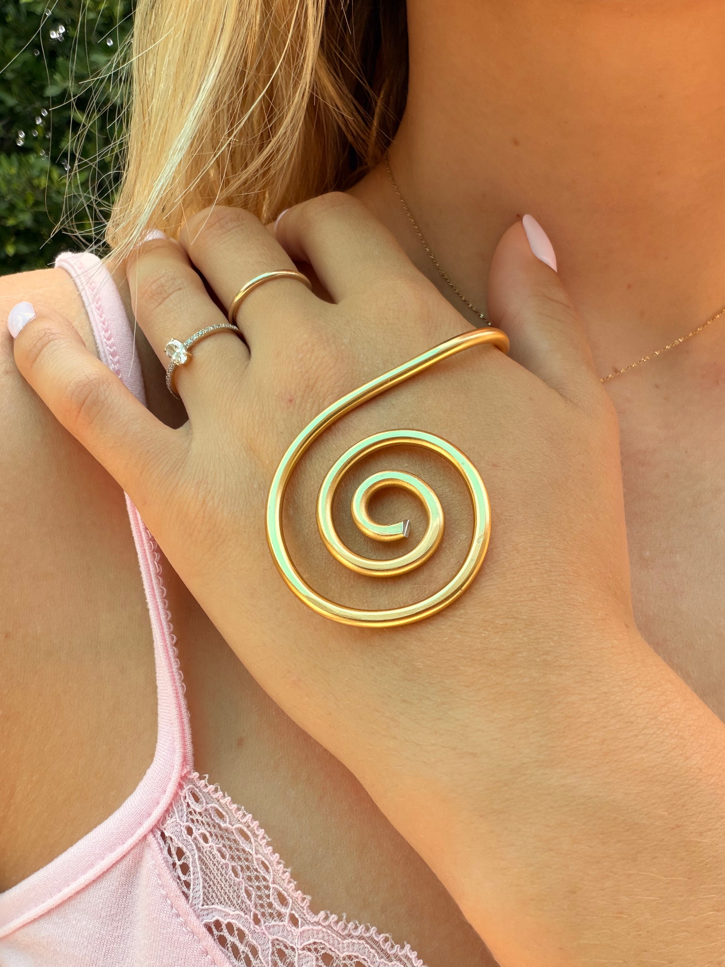 Close-up of a hand wearing a gold spiral ring with a blurred background
