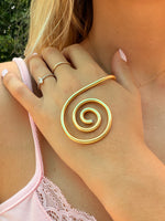 Close-up of a hand wearing a gold spiral ring with a blurred background